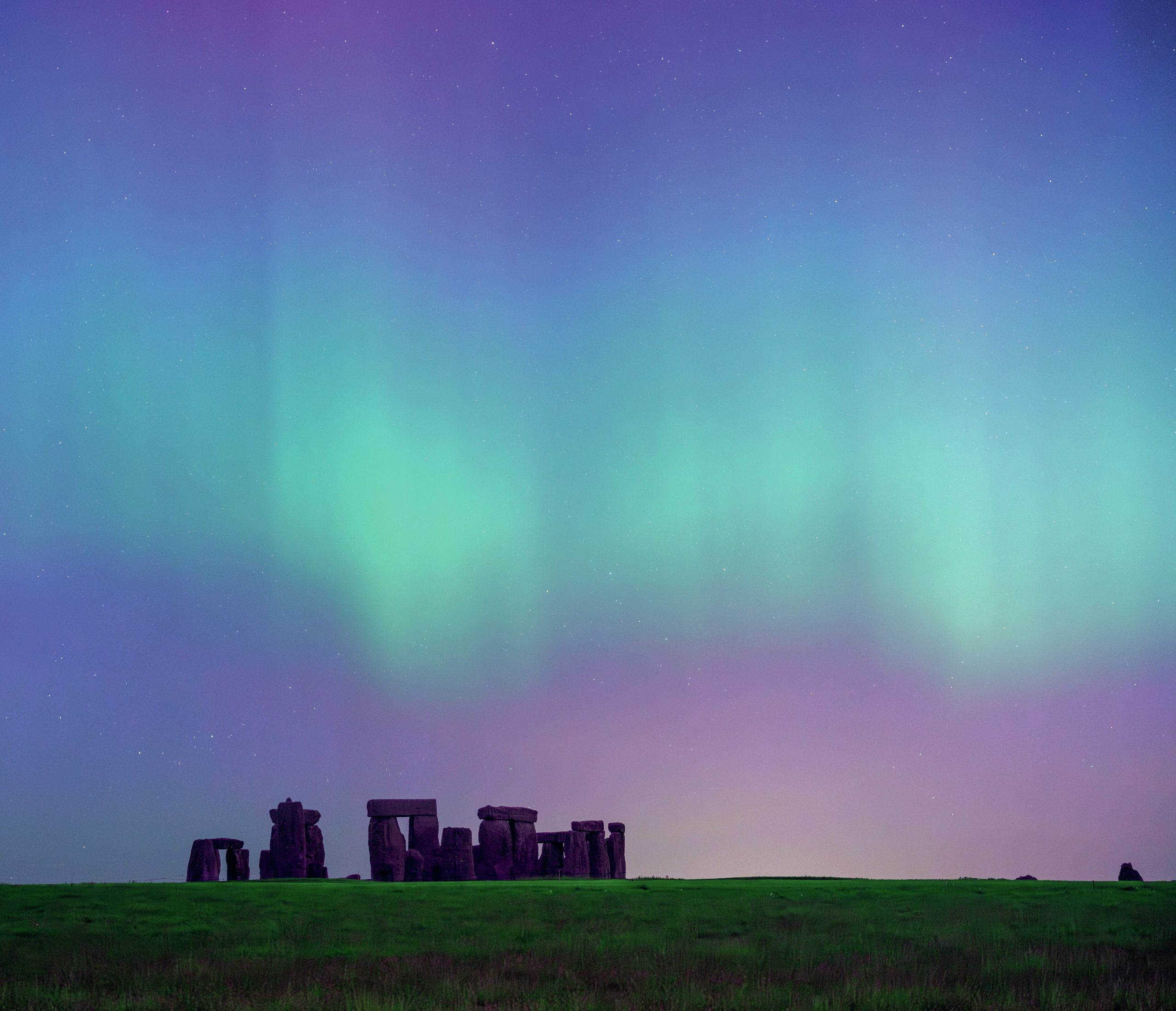 The green lights of the aurora in the sky above the stones of Stonehenge.
