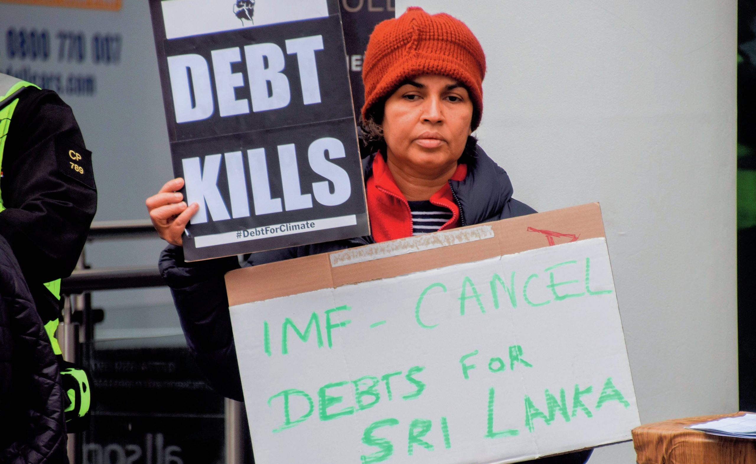 Woman carrying two signs, reading ‘Debt kills’ and ‘IMF – cancel debts for Sri Lanka’.