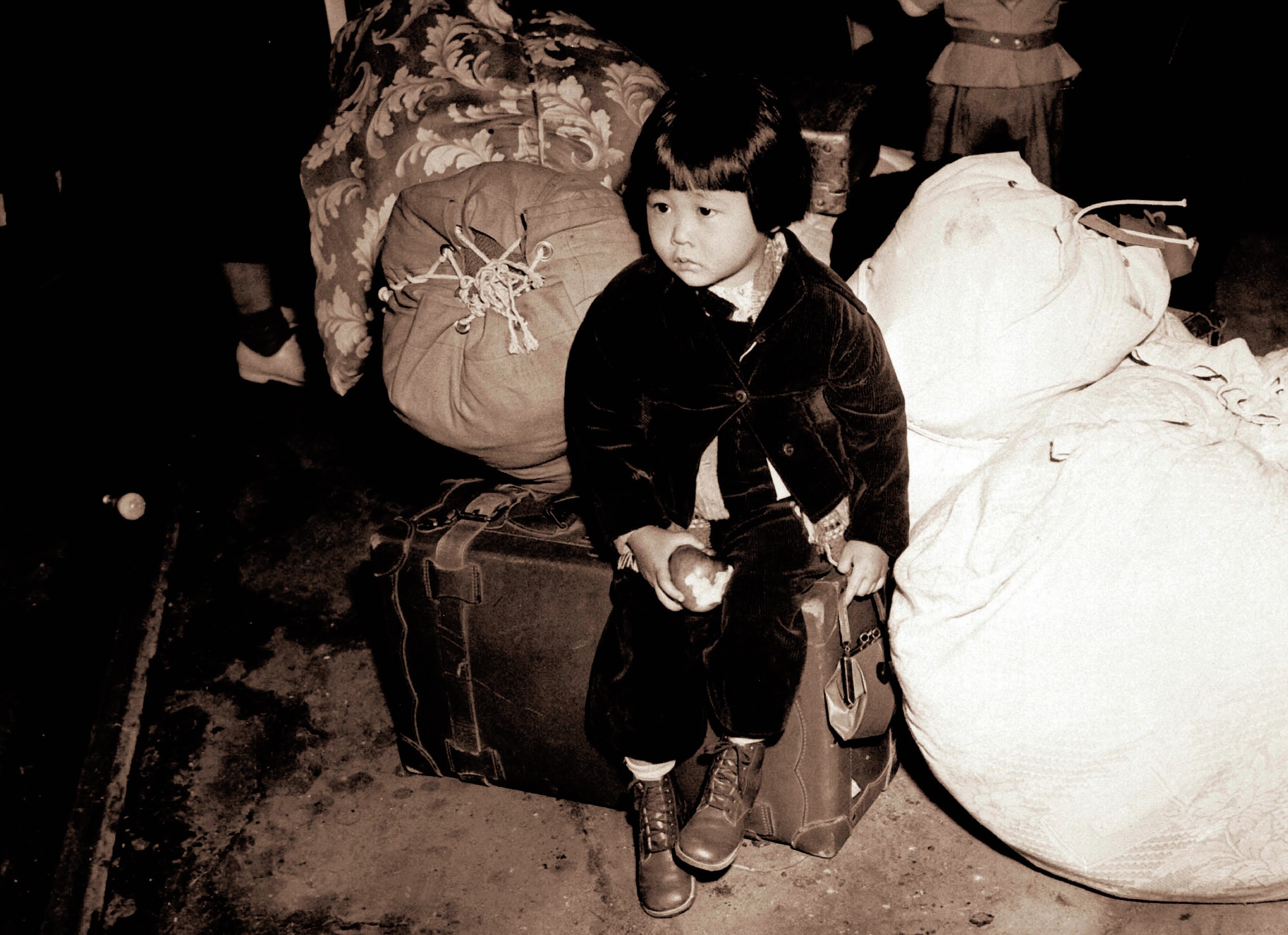 Young girl of Japanese ancestry sitting on a suitcase looking worried.