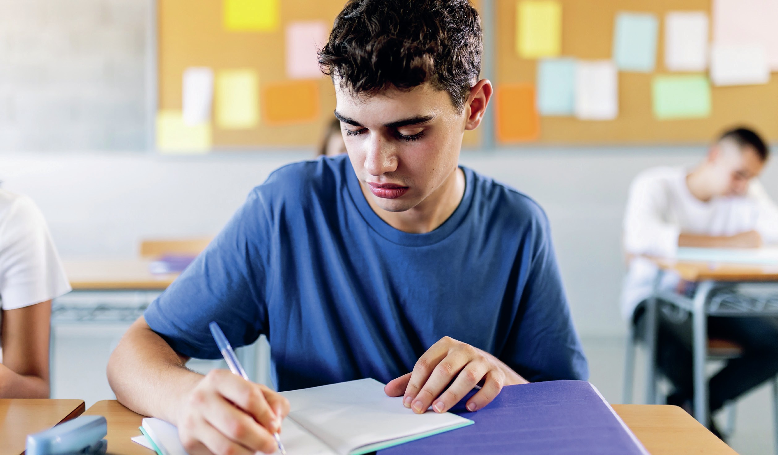 Boy sits at his school desk writing.