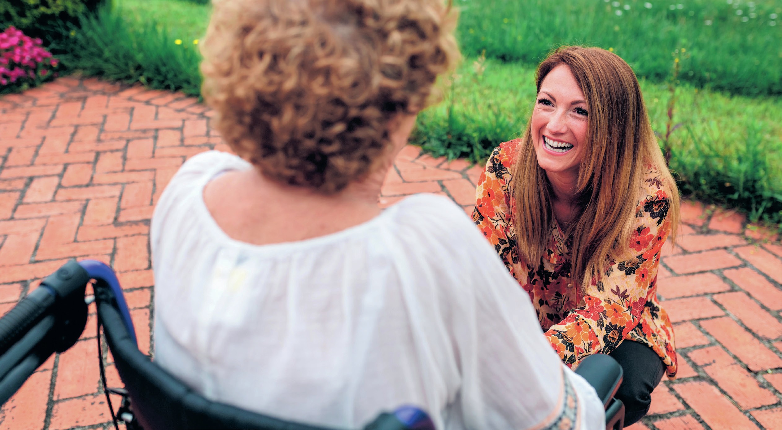 Smiling woman kneels beside a woman in a wheelchair. 