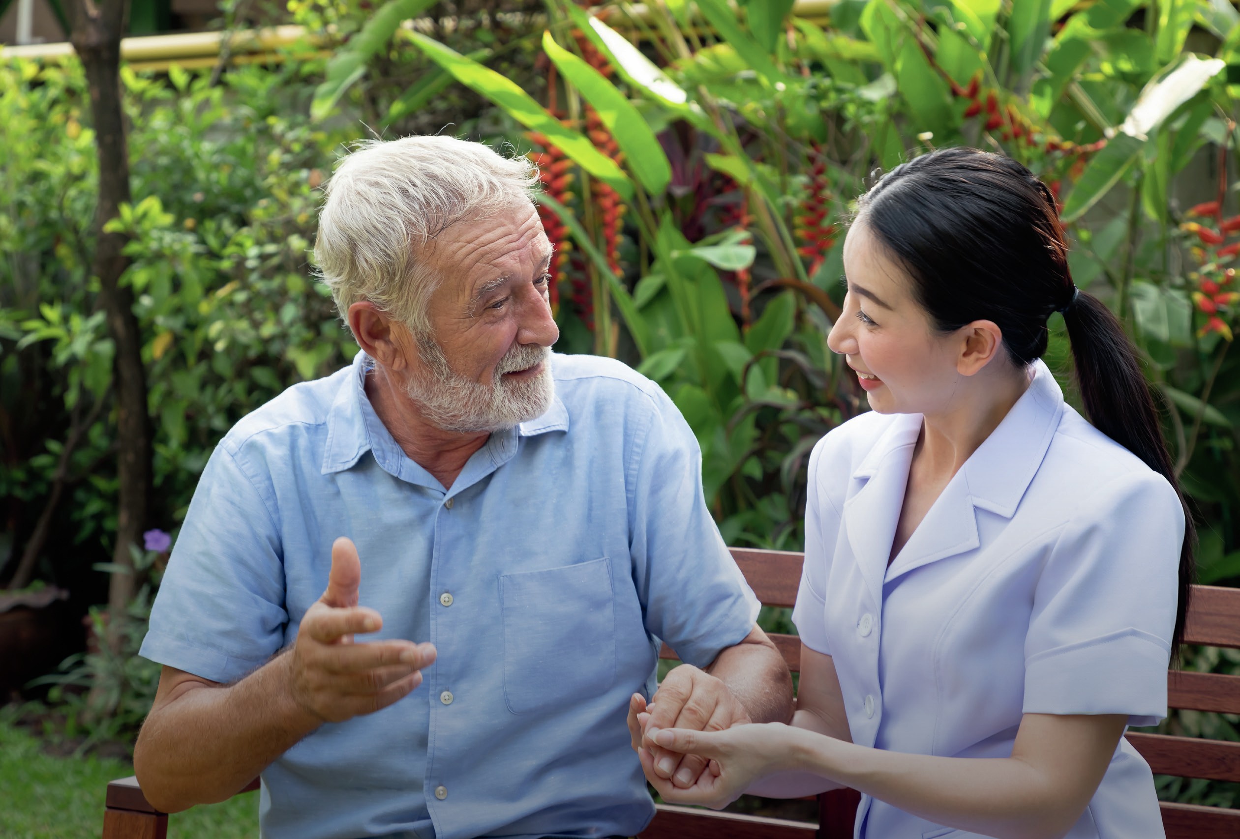 Man and his nurse converse on a bench.