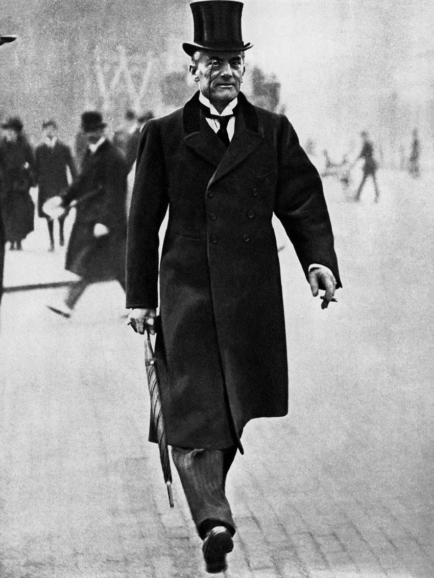 A man wearing a top hat and a black coat walking down the street.