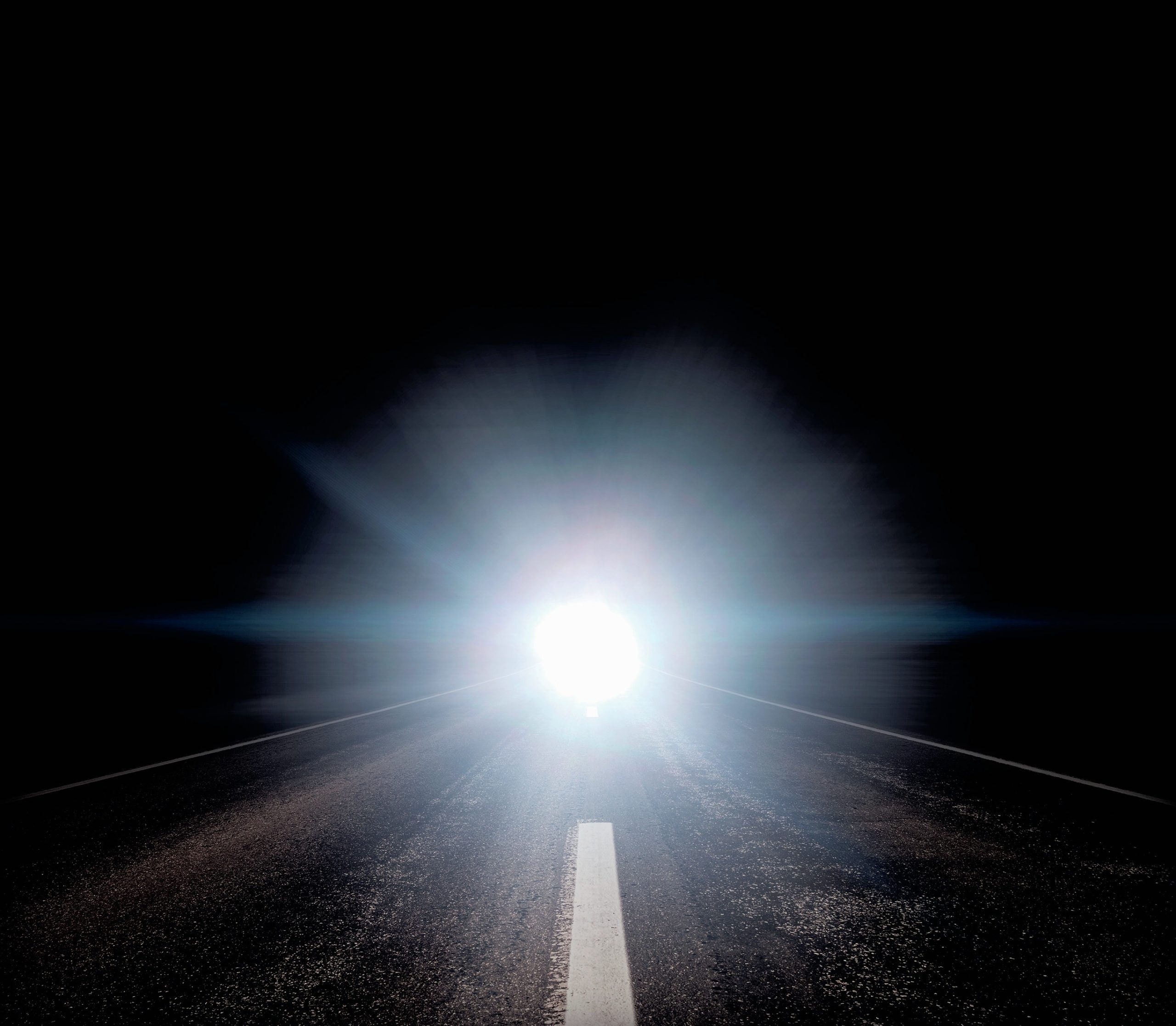 The bright headlights of an oncoming car on a road at night.
