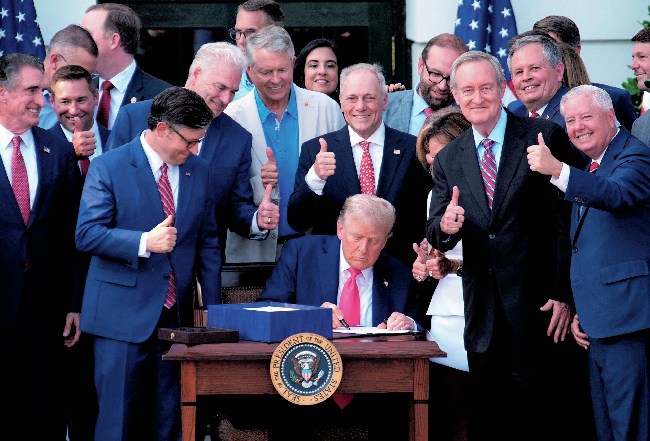 Trump sitting outside the White House signing the bill, surrounded by supporters.