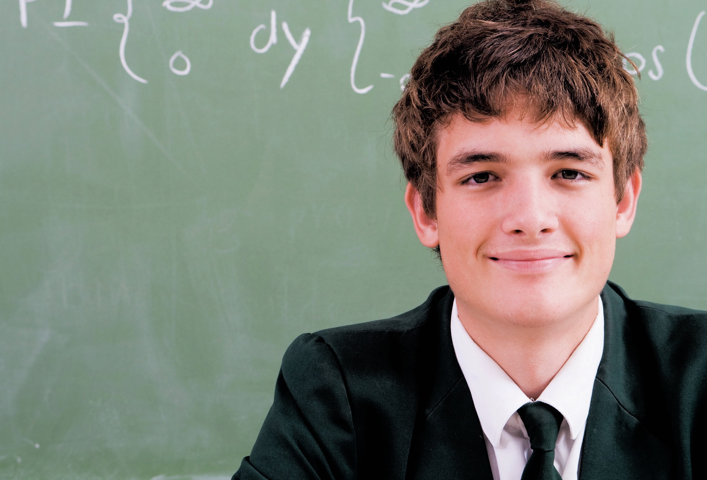 Schoolboy smiling in front of a blackboard.
