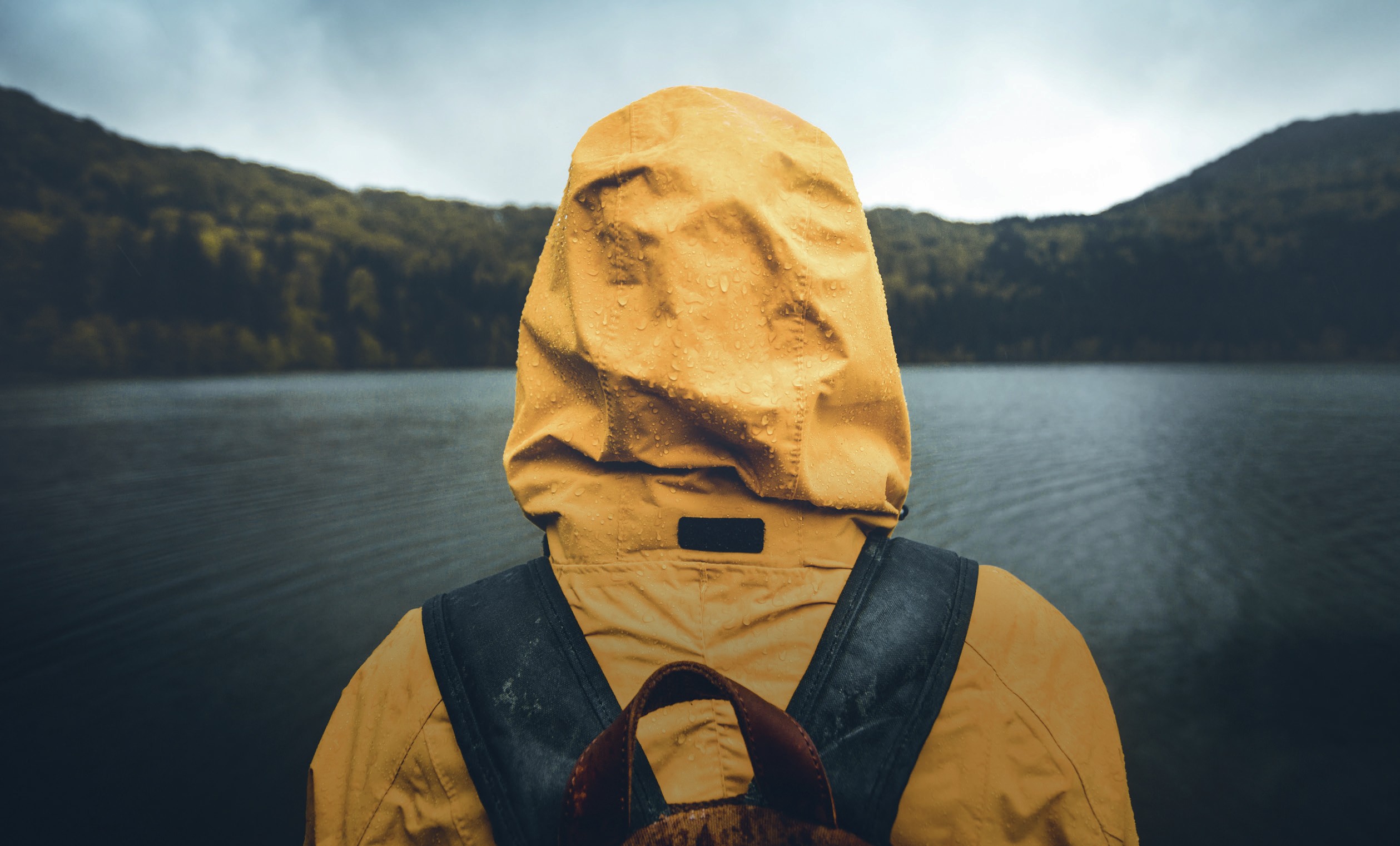 A person standing outside wearing a yellow rain jacket with water droplets on it.