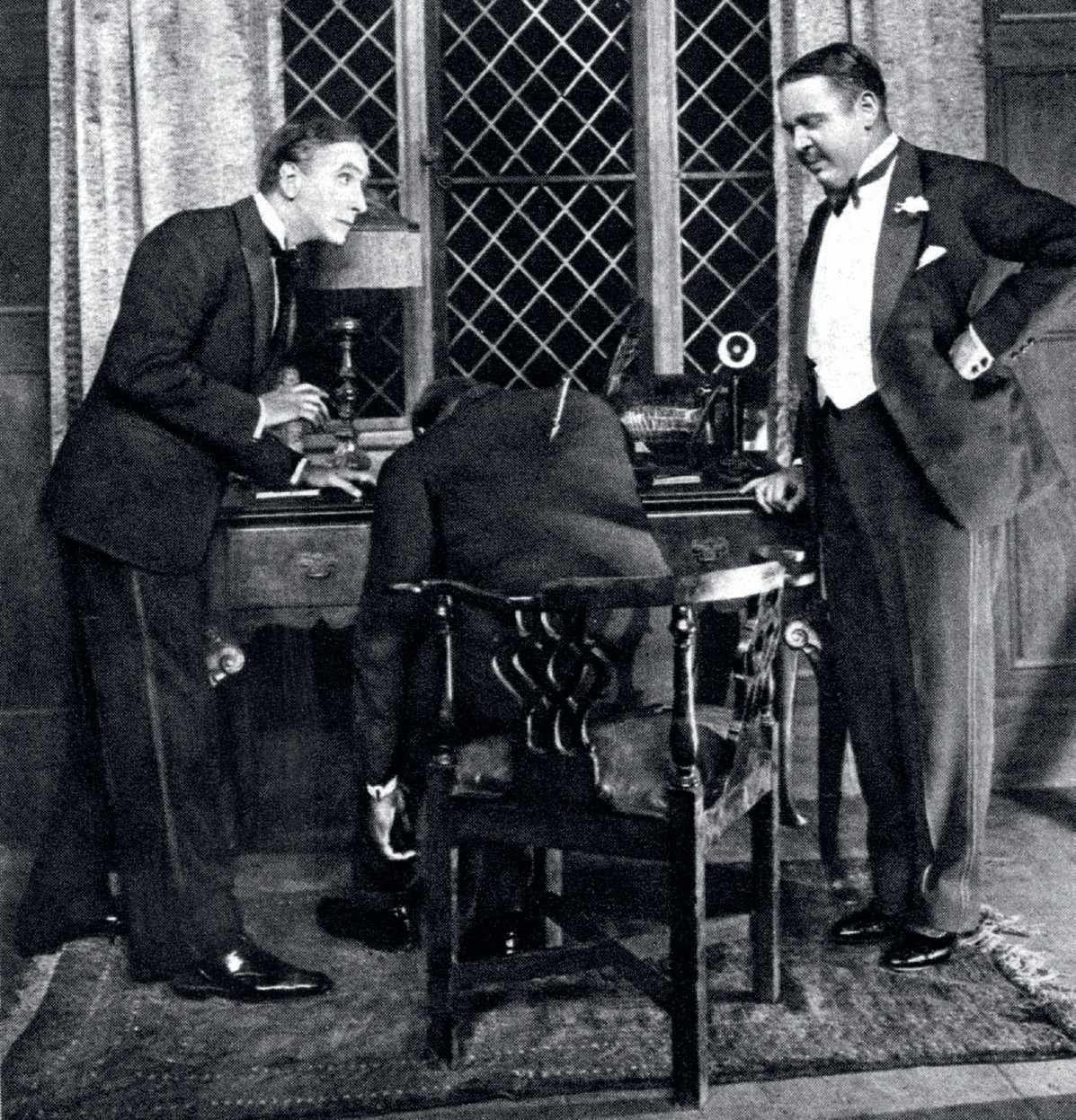 The two men are standing either side of Roger Ackroyd, who is shown from behind, slumped at a desk with a dagger sticking out of his back.