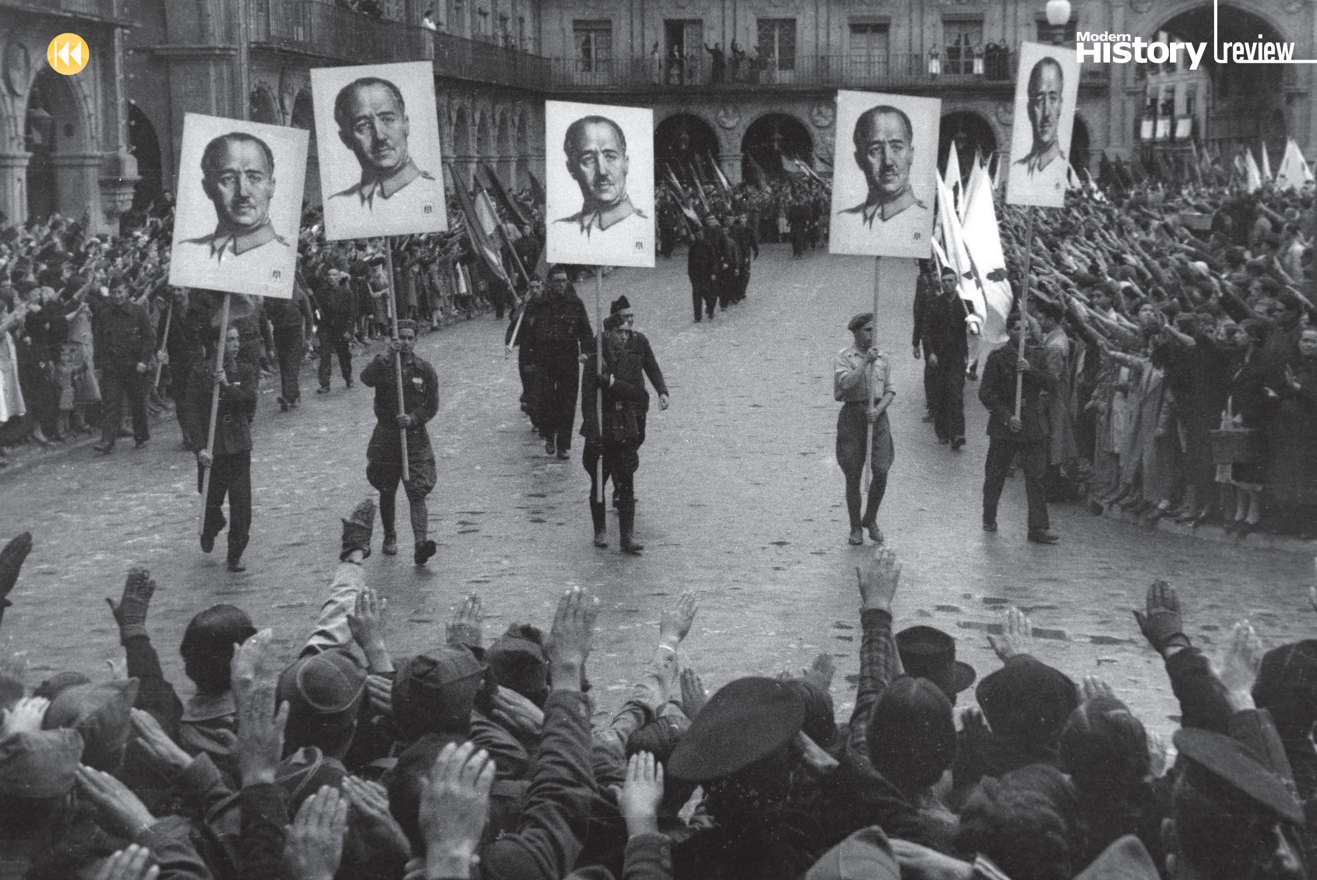 Crowds cheer a group of men in military dress, holding placards with a man’s face on them