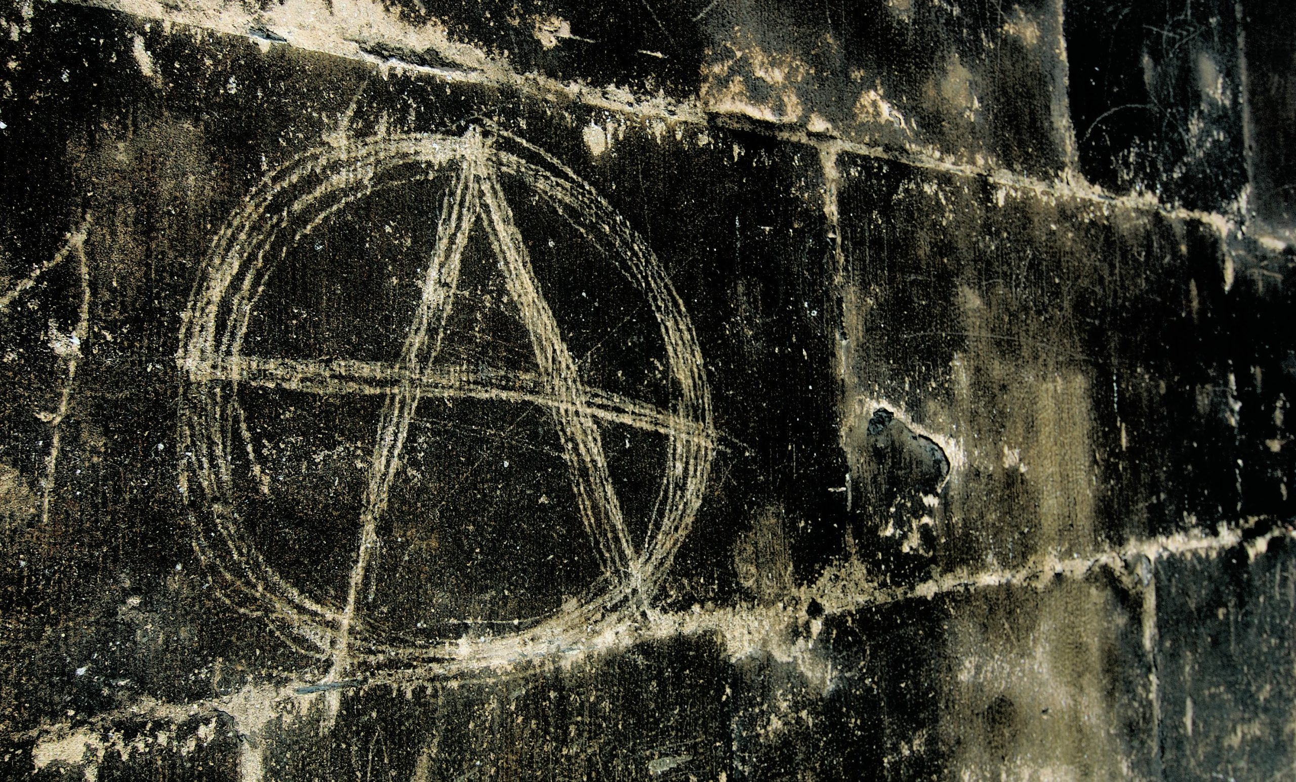 Anarchy symbol (capital A with a circle around it) chalked onto a wall.
