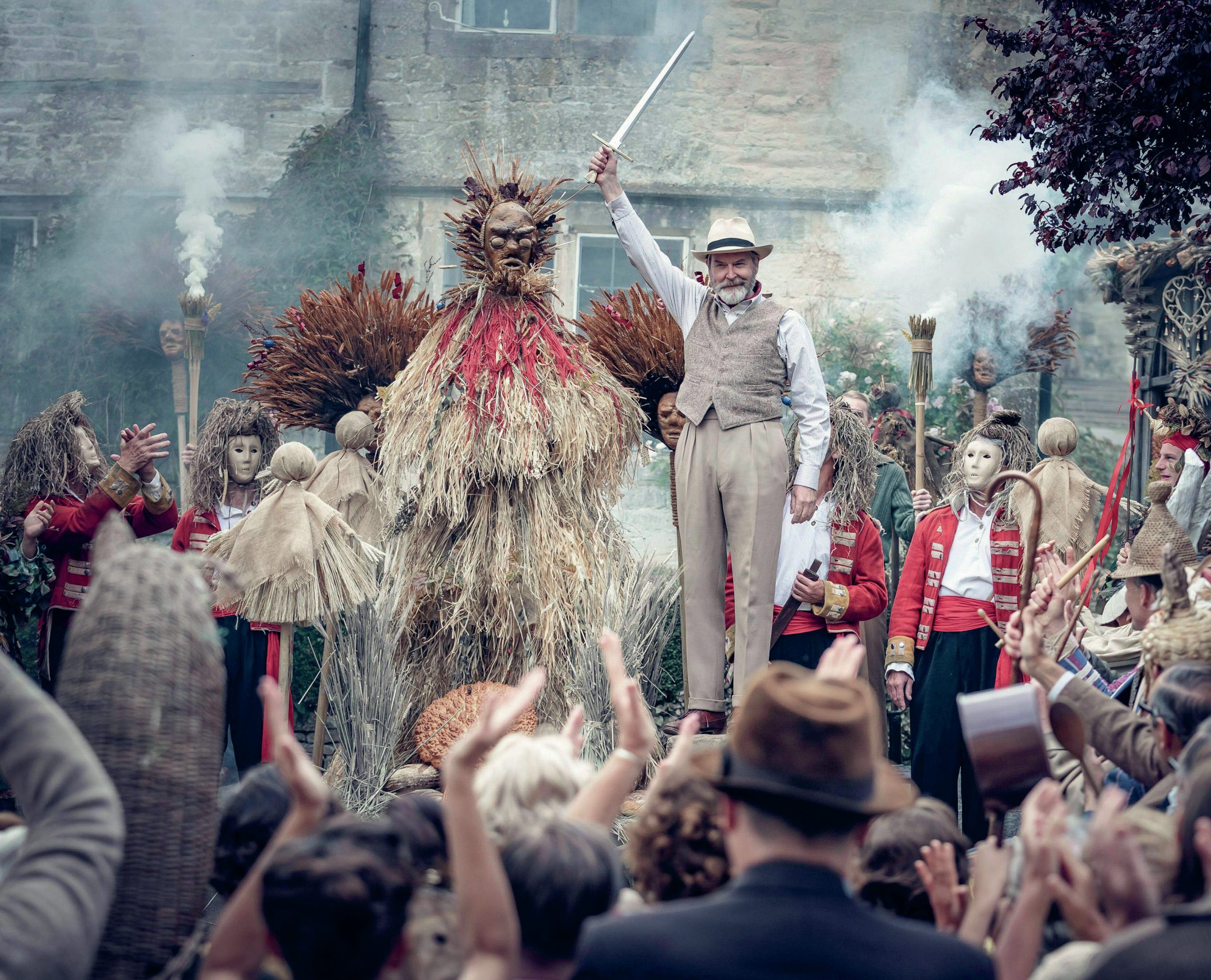 Supernatural gathering in a village, with people wearing masks.