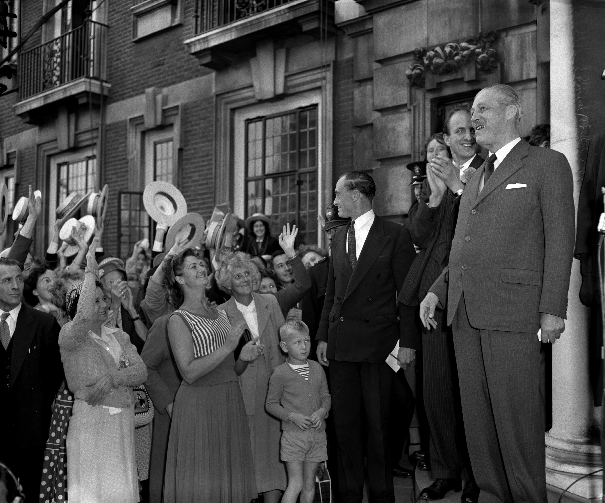 A man in a suit is cheered by a crowd waving their hats.