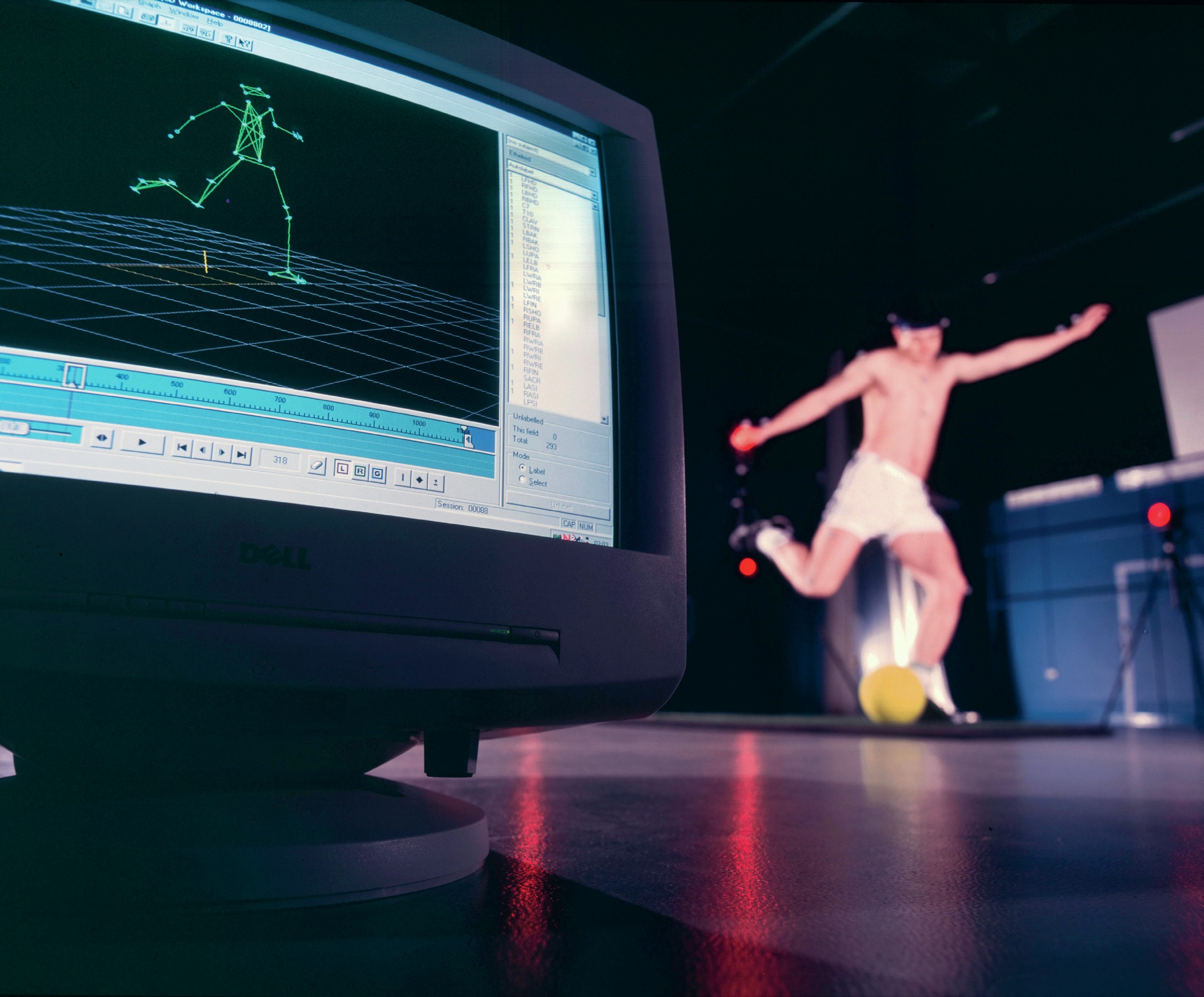 A computer shows a digitalised image of a person kicking a ball. A person wearing sensors kicks a ball nearby
