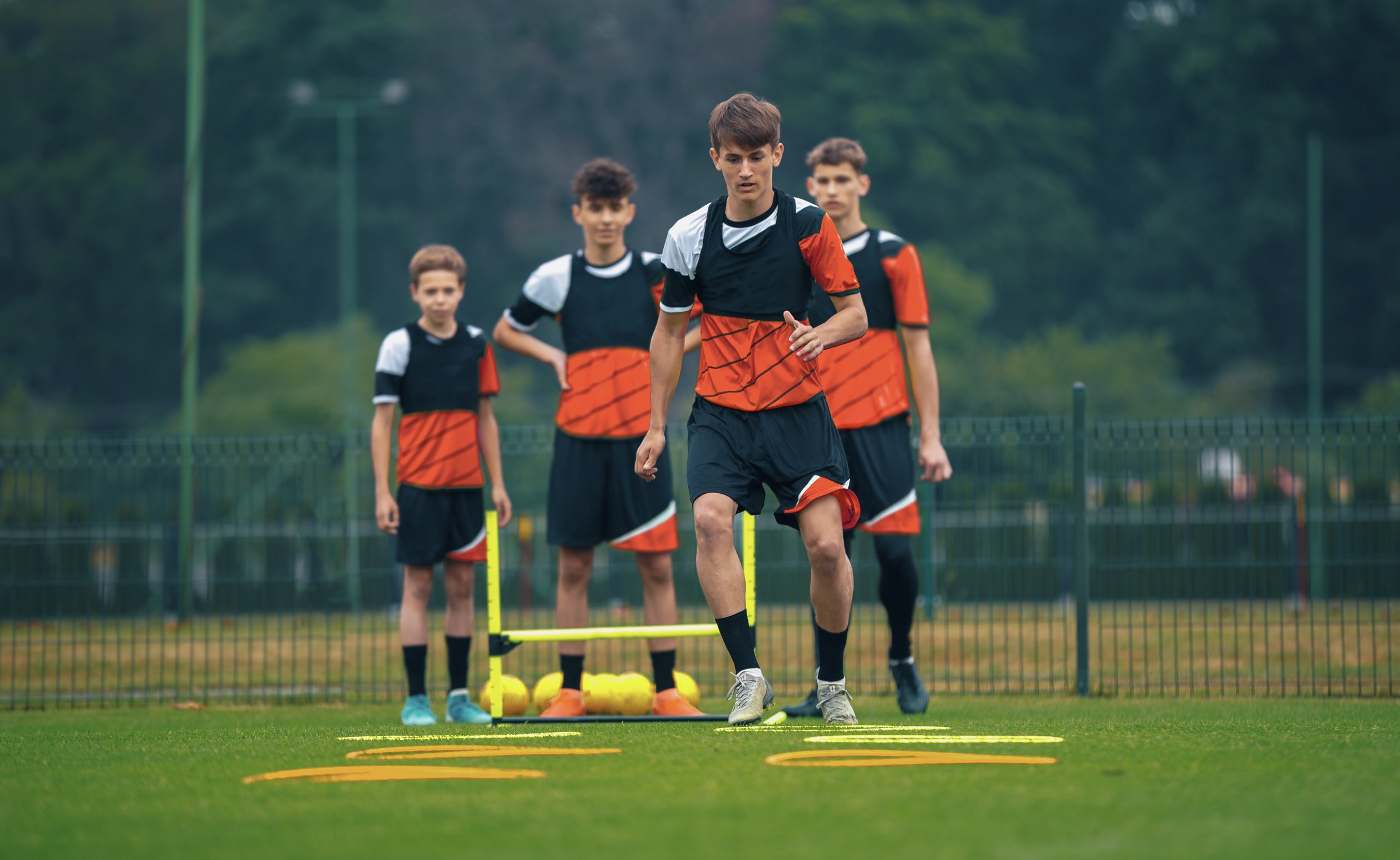Four boys of different heights doing training exercises in a sports field.