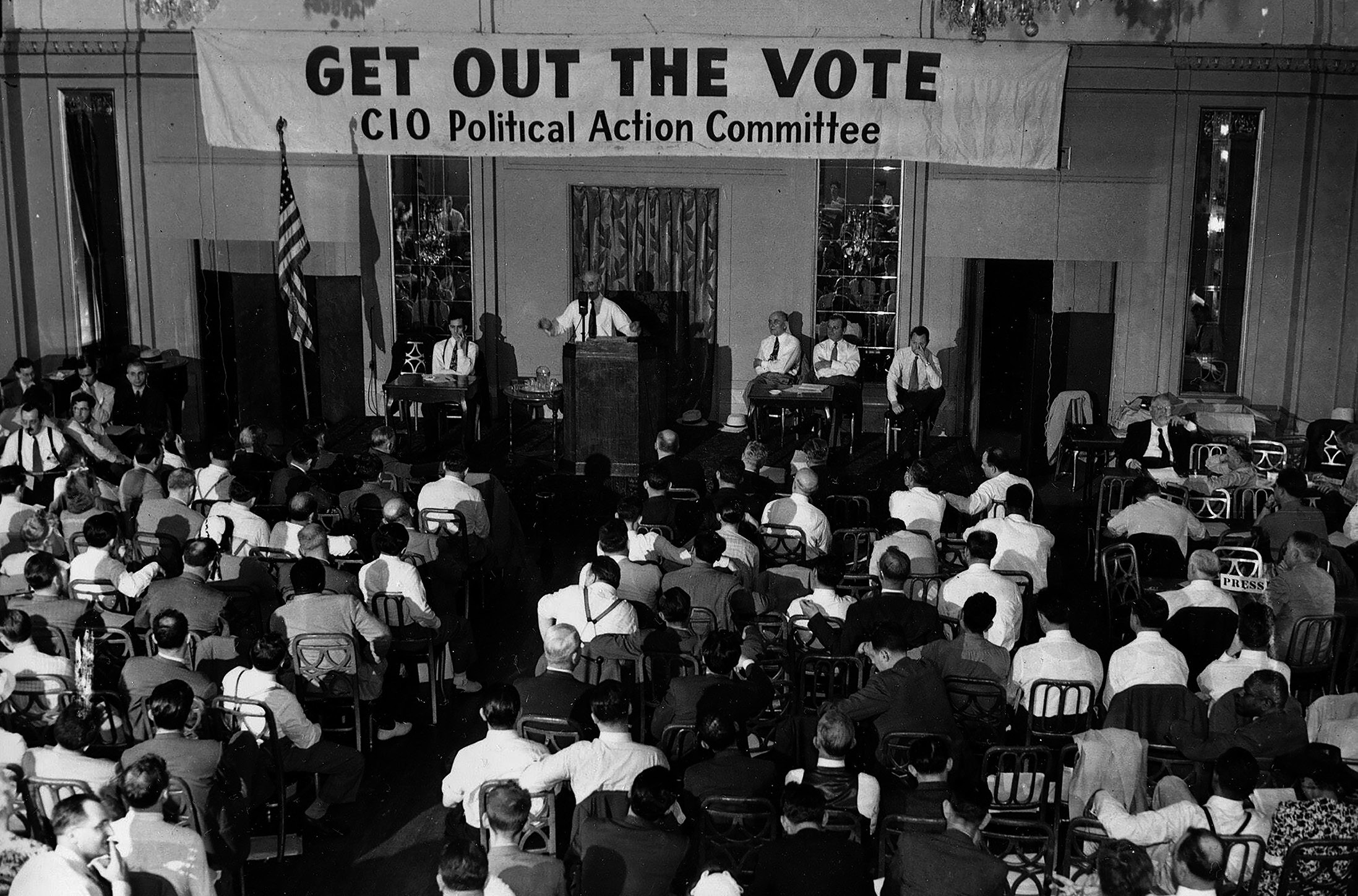 Black and white photo of Murray at a lectern, talking to a room of people. The banner above him reads ‘Get out the vote: CIO Political Action Committee’.